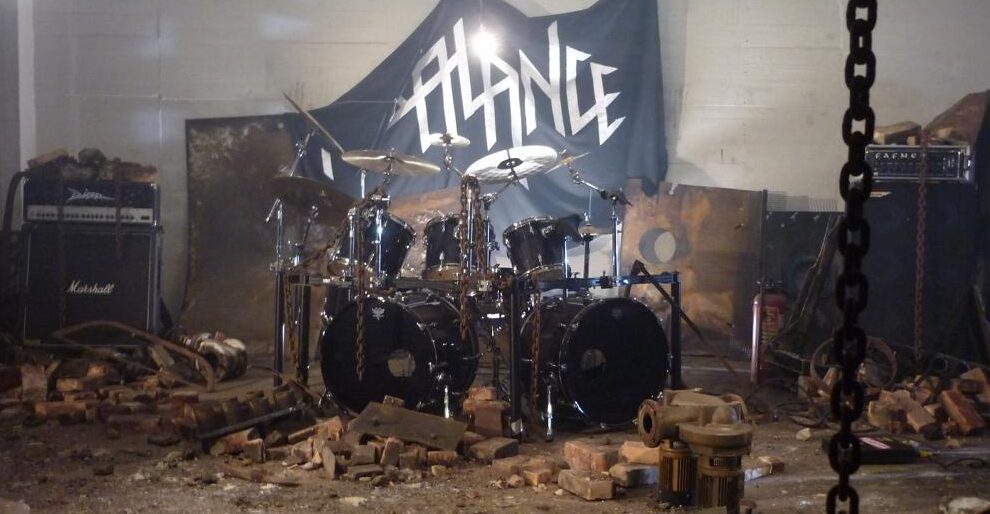A drumset, amps and a falling banner with the Imbalance logo in a pile of ruins